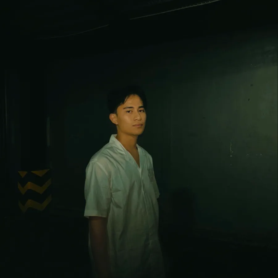 Portrait of Fadhil Muhammad in a white shirt against a dark green wall